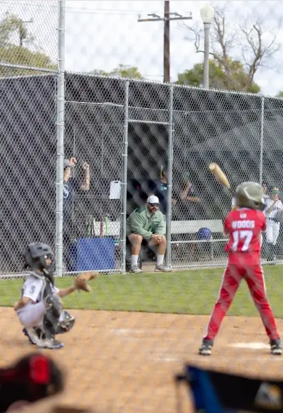 Young batter at the plate with coach watching from the dugout during a game